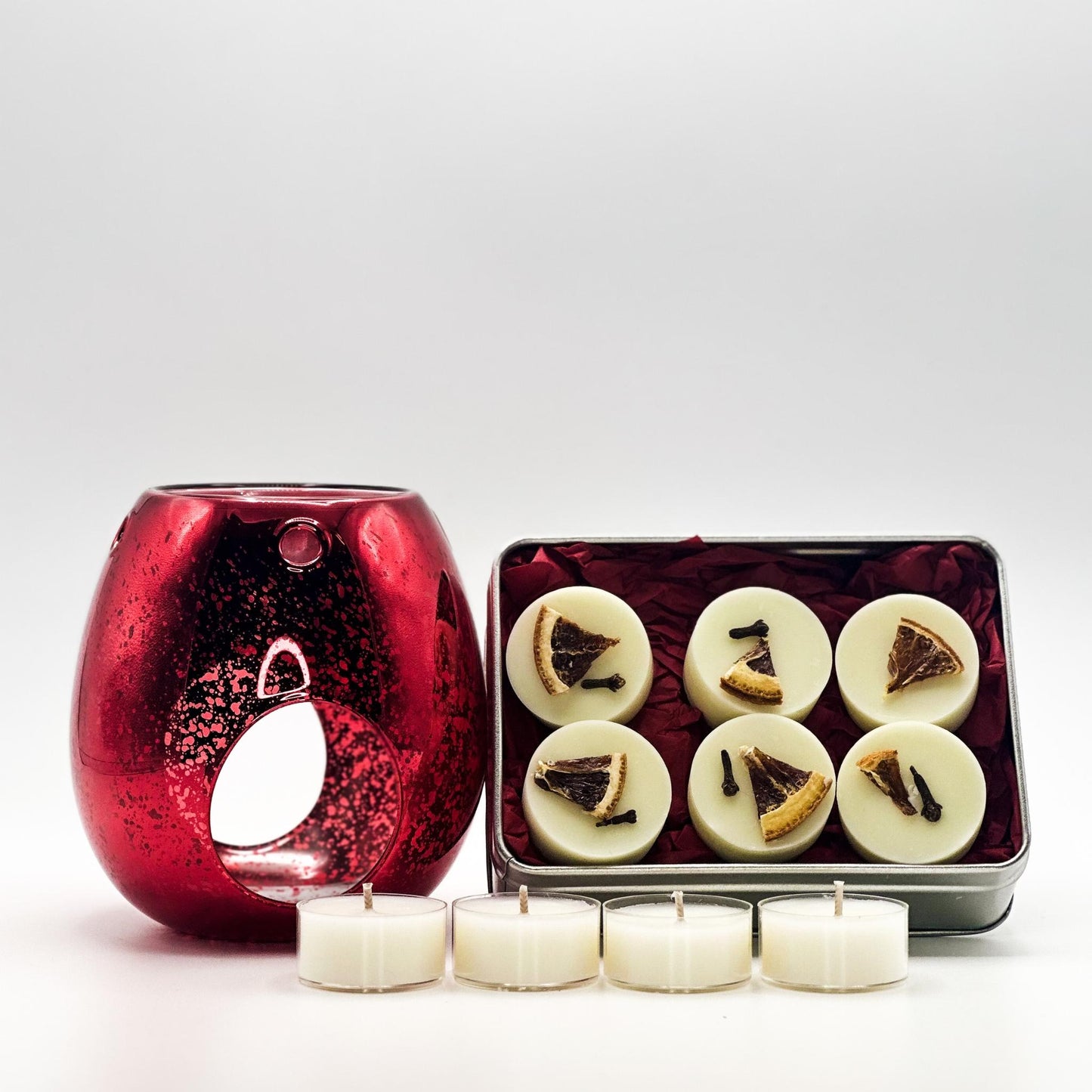 Red candle warmer with six white candles and a small tin of more candles on a white background