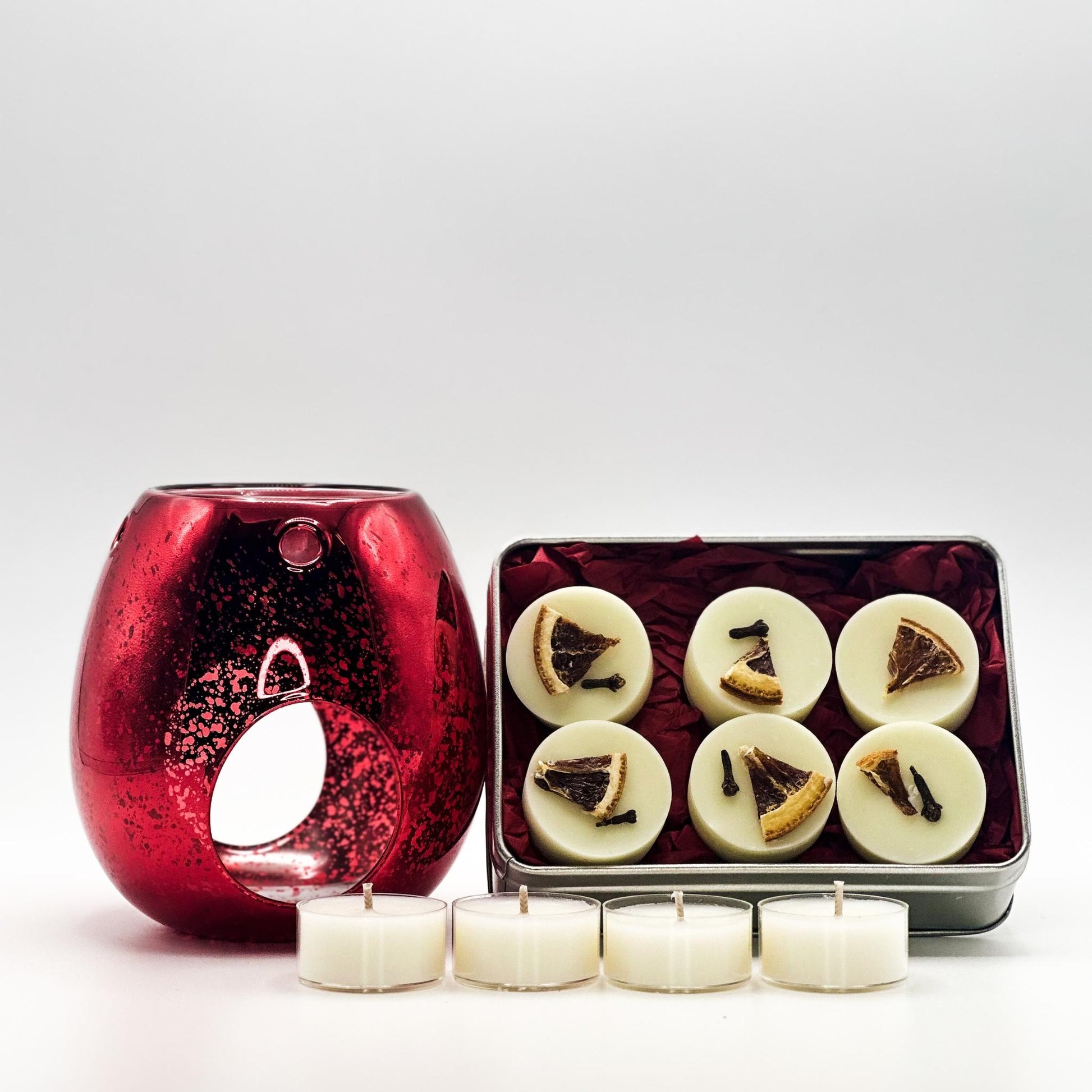 Red candle warmer with six white candles and a small tin of more candles on a white background