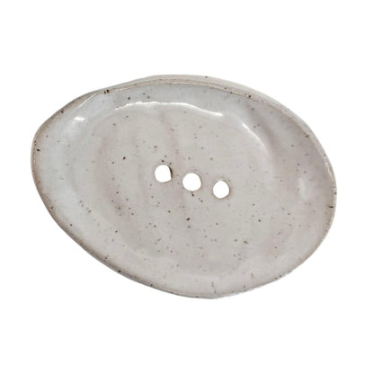An organic-shaped ceramic dish with three holes, featuring a speckled off-white glaze on a solid white background.